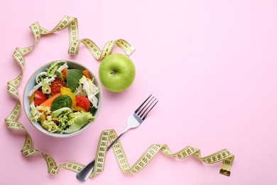 Measuring tape, salad, apple and fork on pink background, flat lay. Space for text