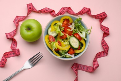 Photo of Measuring tape, salad, apple and fork on pink background, flat lay