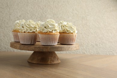 Tasty vanilla cupcakes with cream on wooden table, space for text