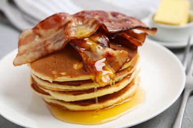 Photo of Delicious pancakes with maple syrup and fried bacon on grey table, closeup