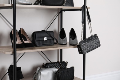 Shelving unit with stylish shoes and purses near white wall. Element of dressing room interior