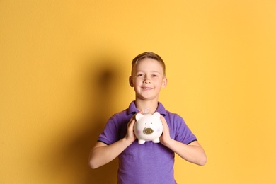 Little boy with piggy bank on color background