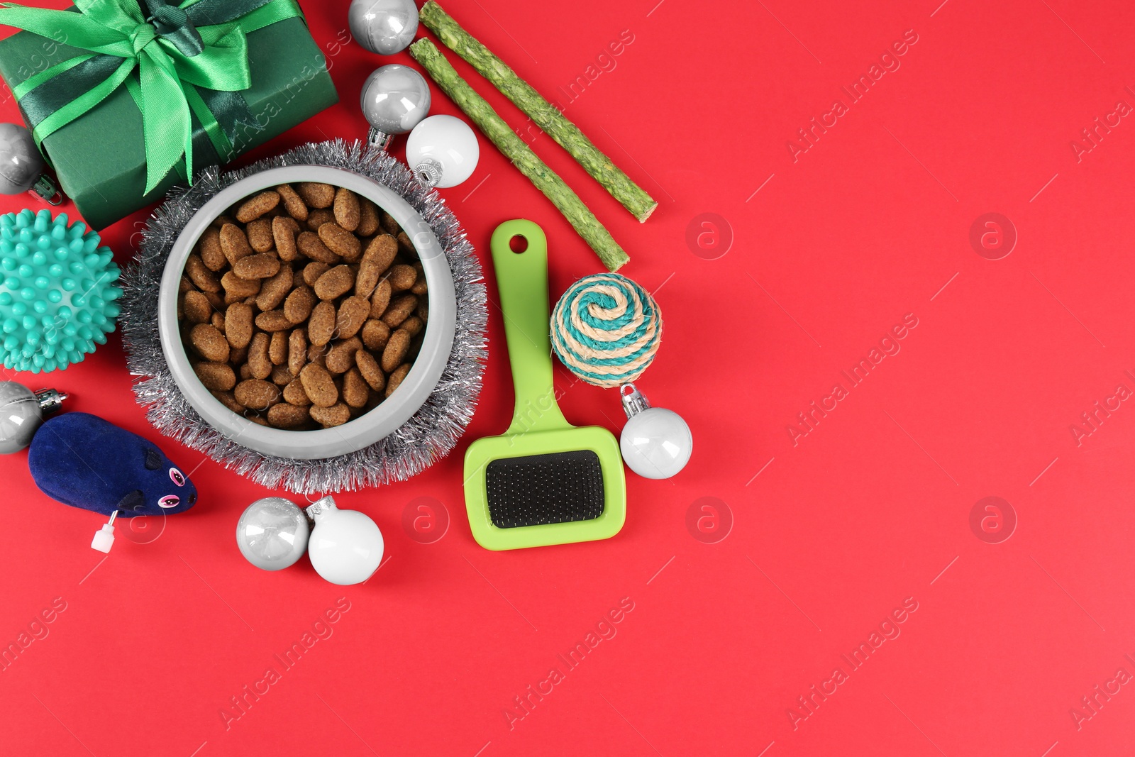 Photo of Different pet goods with Christmas gift on red background, flat lay and space for text. Shop assortment