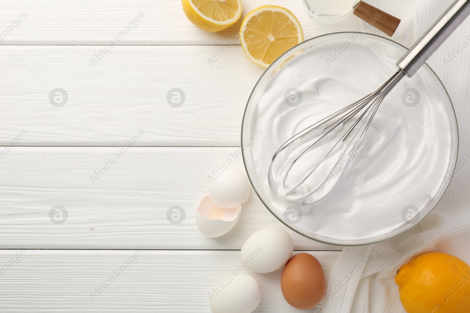 Photo of Bowl with whipped cream, whisk and ingredients on white wooden table, flat lay. Space for text