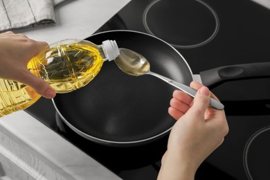 Photo of Woman with spoon pouring cooking oil into frying pan on stove, closeup