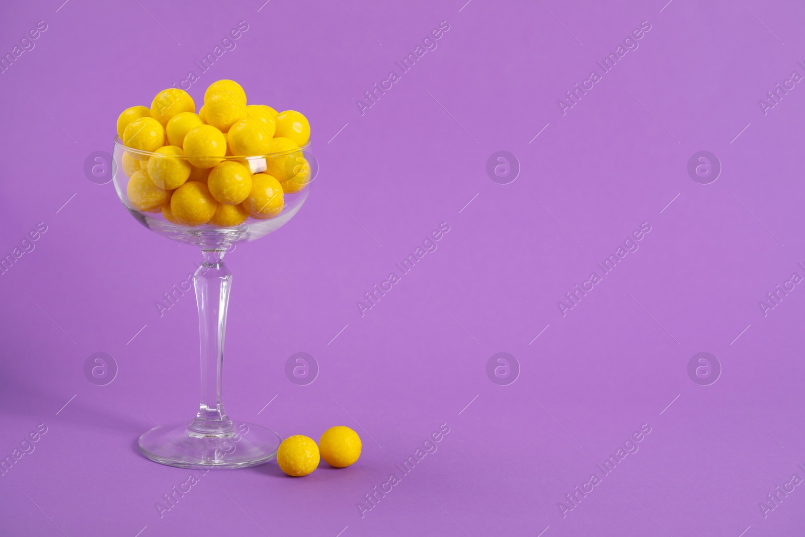 Photo of Tasty lemon chewing gums in glass on purple background. Space for text