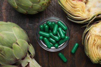 Photo of Bowl with pills and fresh artichokes on wooden table, flat lay