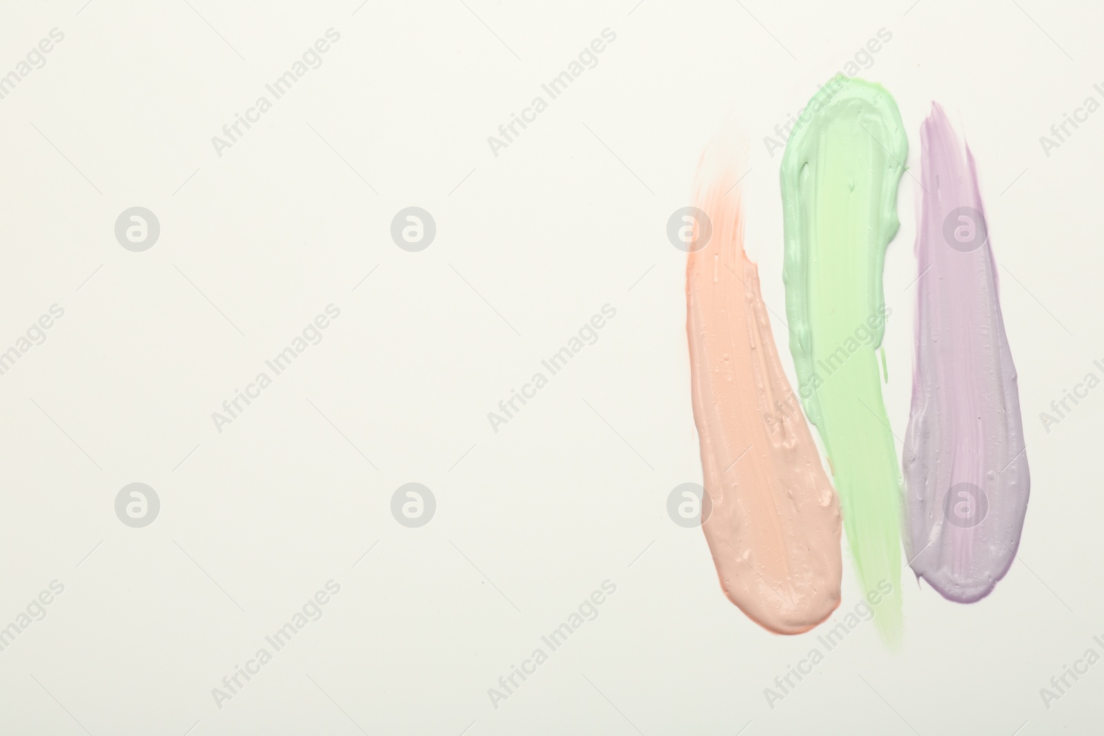 Photo of Strokes of pink, green and purple color correcting concealers on white background, top view