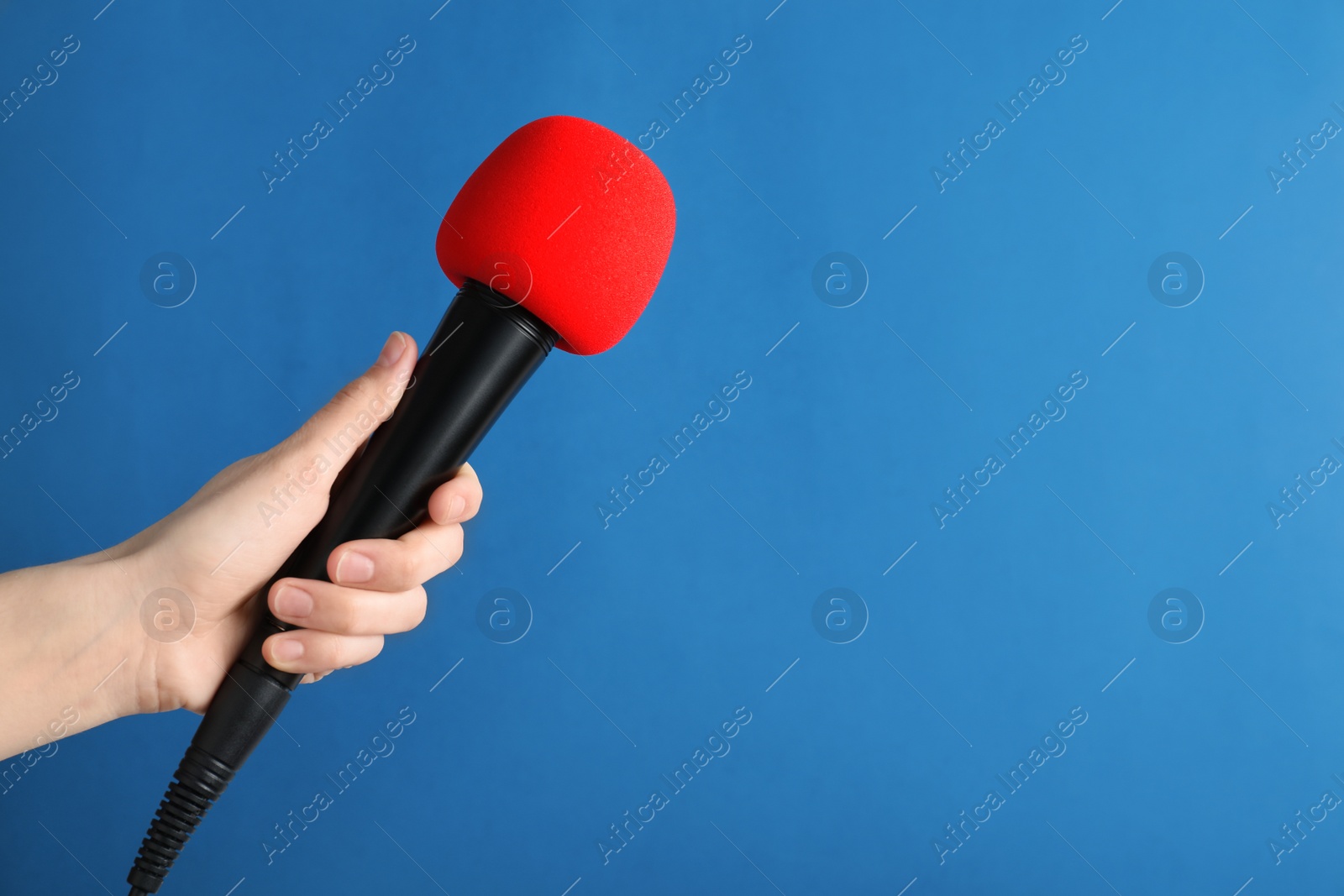 Photo of Woman holding modern microphone on color background, closeup. Space for text