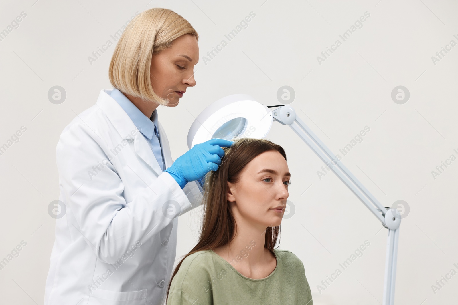 Photo of Trichologist examining patient`s hair under lamp in clinic