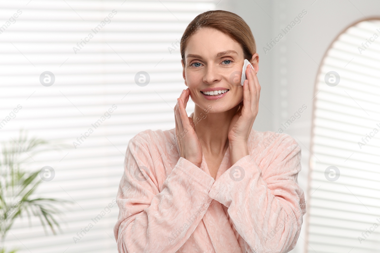 Photo of Beautiful woman removing makeup with cotton pad indoors