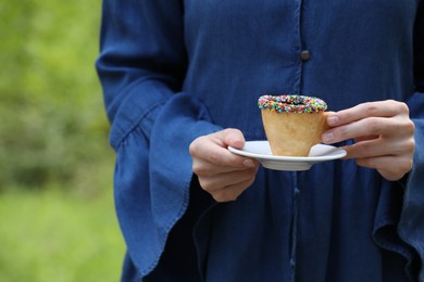 Woman with delicious edible biscuit cup of coffee decorated with sprinkles outdoors, closeup. Space for text