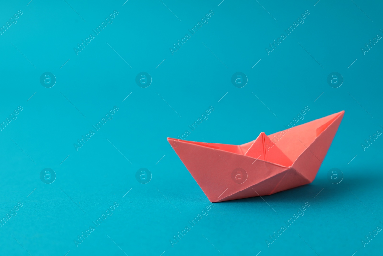 Photo of Handmade pink paper boat on light blue background.  Space for text
