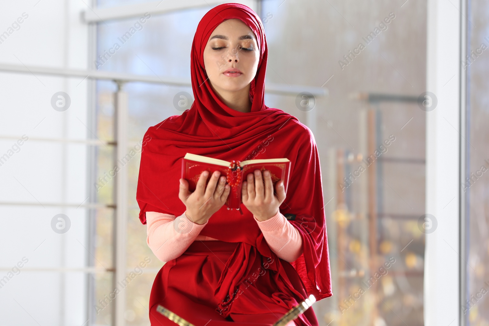 Photo of Muslim woman in hijab reading Koran indoors