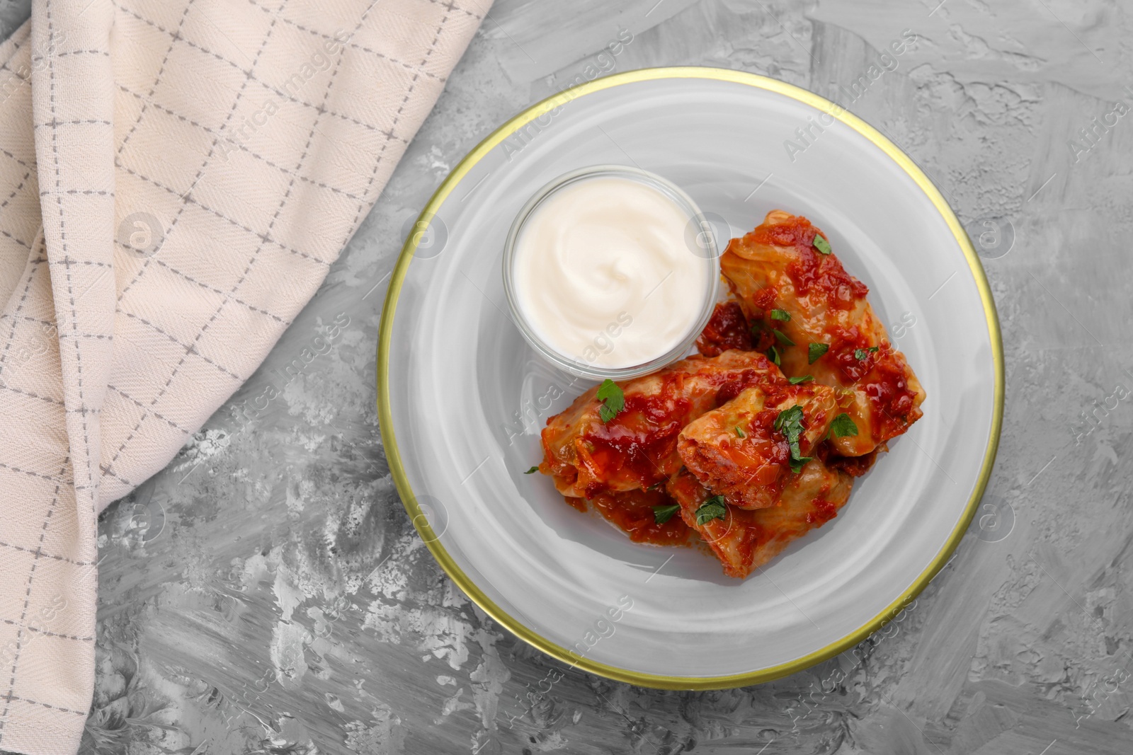 Photo of Delicious stuffed cabbage rolls served with sour cream on grey textured table, top view