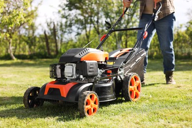 Photo of Man cutting green grass with lawn mower in garden, selective focus