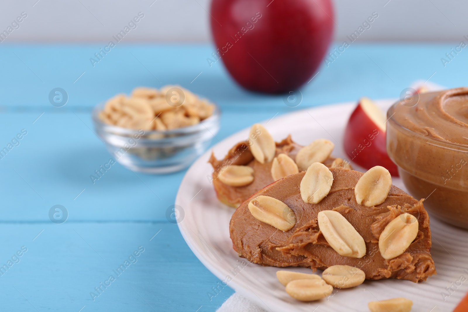 Photo of Slices of fresh apple with peanut butter and nuts on light blue wooden table, closeup. Space for text