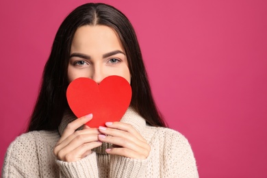 Photo of Portrait of young woman with paper heart on color background. Space for text