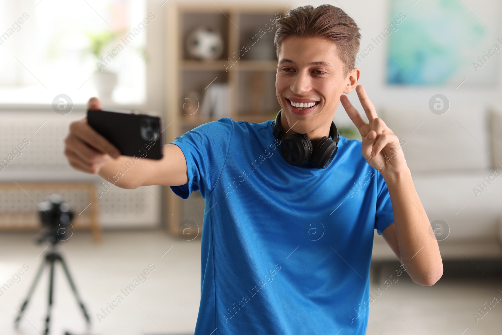 Photo of Smiling sports blogger streaming online fitness lesson with smartphone at home