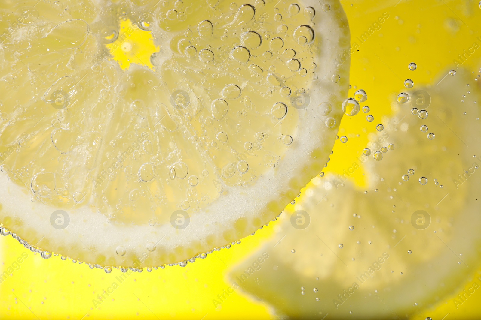 Photo of Juicy lemon slices in soda water against yellow background, closeup