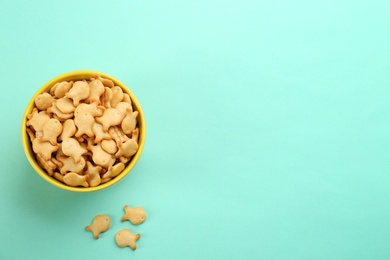 Photo of Delicious goldfish crackers in bowl on turquoise background, flat lay. Space for text