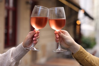 Photo of Women clinking glasses with rose wine outdoors, closeup