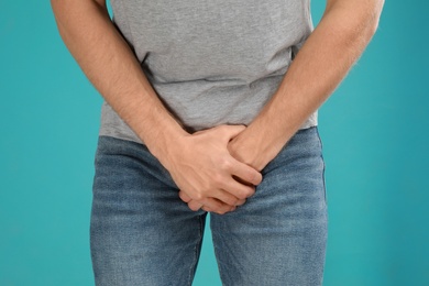 Photo of Man suffering from pain on turquoise background, closeup. Urology problems