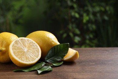 Photo of Fresh lemons and green leaves on wooden table outdoors, closeup. Space for text