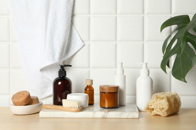 Different bath accessories and personal care products on wooden table near white tiled wall