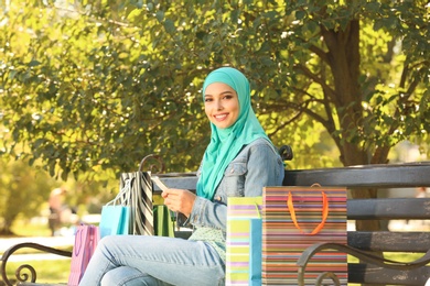 Muslim woman with mobile phone sitting on bench in park