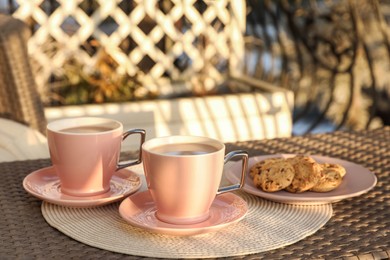 Cups with tasty cocoa and cookies on rattan table at balcony