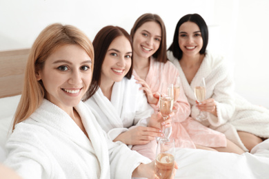 Photo of Beautiful young ladies with champagne taking selfie on bed at pamper party. Women's Day