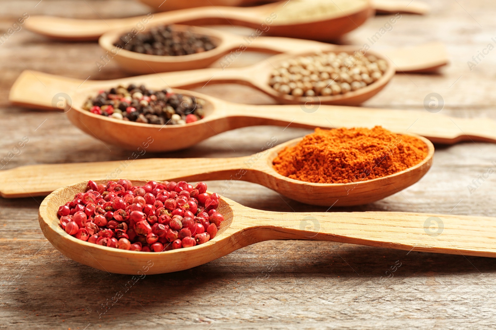 Photo of Spoons with different types of pepper on wooden table