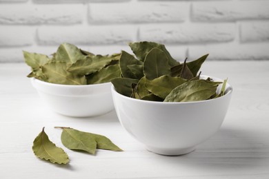 Photo of Dry bay leaves in bowls on white wooden table, closeup