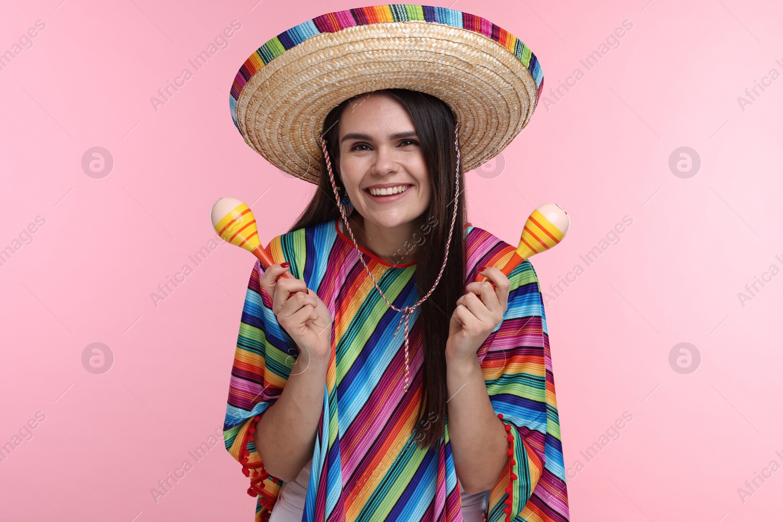 Photo of Young woman in Mexican sombrero hat and poncho with maracas on pink background