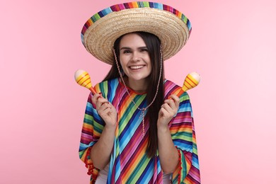 Photo of Young woman in Mexican sombrero hat and poncho with maracas on pink background