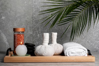 Photo of Herbal massage bags, spa stones, sea salt, rolled towel and candle on grey table