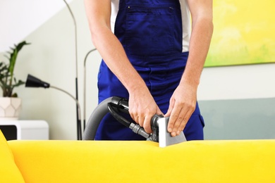 Photo of Dry cleaning worker removing dirt from sofa indoors