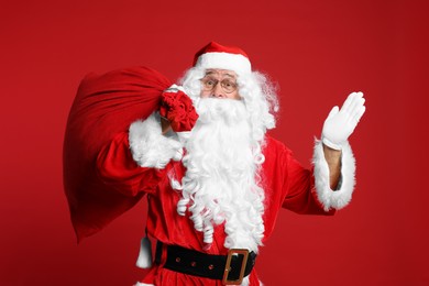 Photo of Santa Claus with bag of Christmas presents waving hello on red background