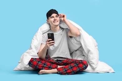 Photo of Happy man in pyjama wrapped in blanket using smartphone on light blue background
