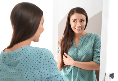 Young woman looking at her reflection in mirror on white background