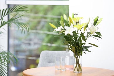 Vase with bouquet of beautiful lilies on wooden table indoors. Space for text