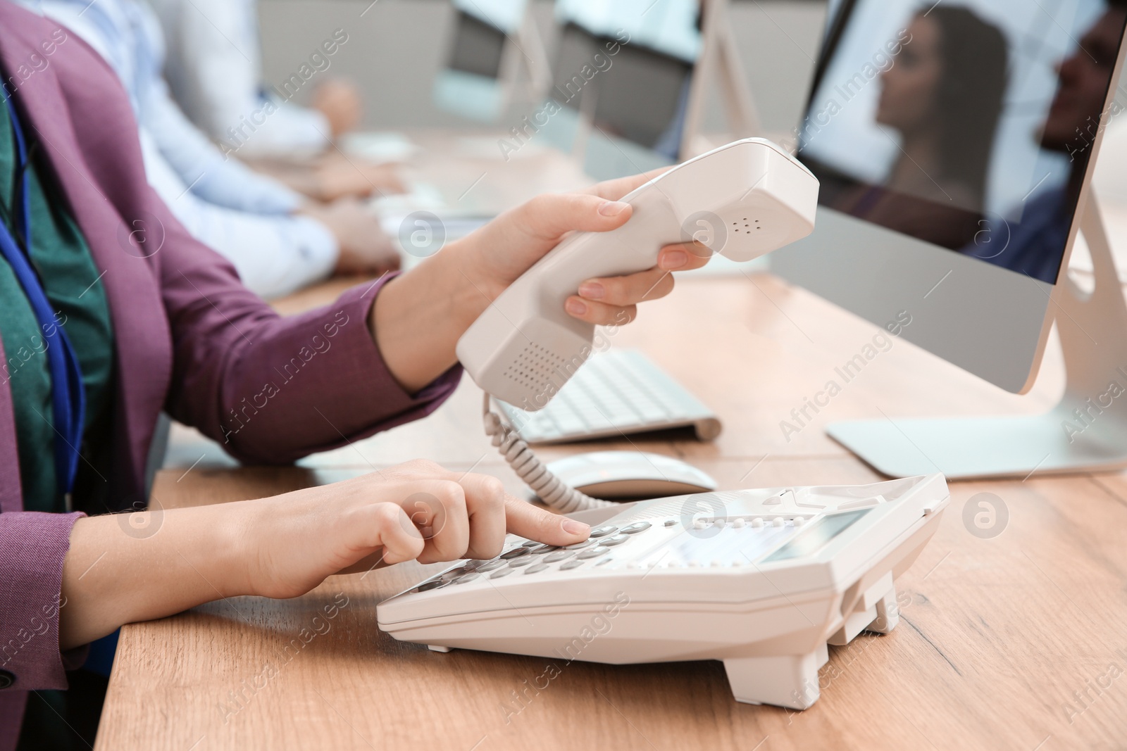 Photo of Technical support operator dialing number on telephone at table, closeup