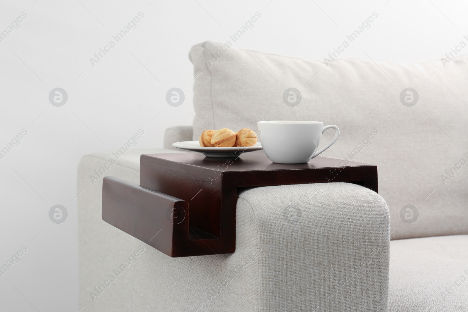 Photo of Cup of coffee and nut shaped cookies on sofa with wooden armrest table indoors. Interior element