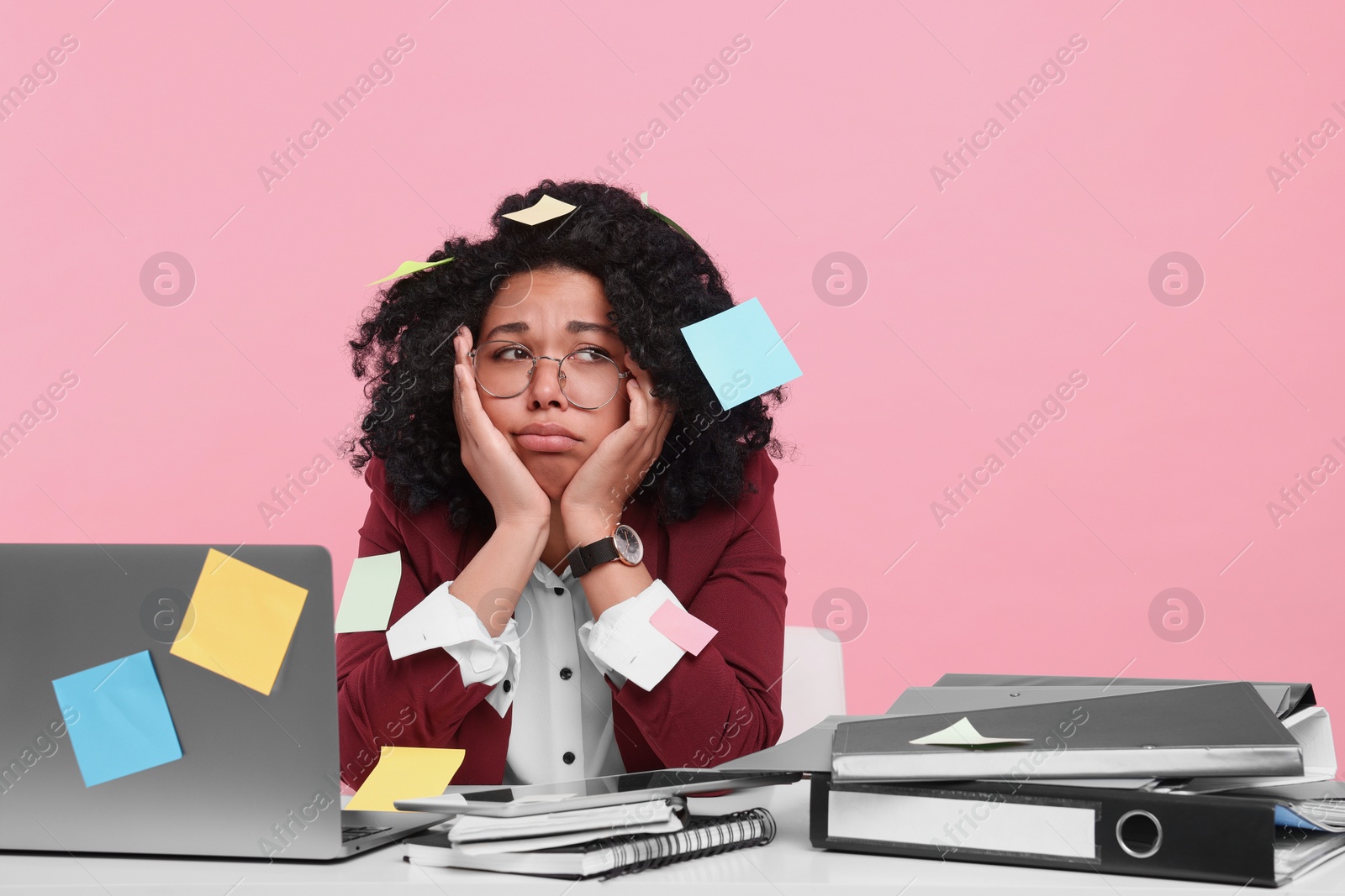 Photo of Stressful deadline. Exhausted woman sitting at white table against pink background. Sticky notes everywhere as reminders