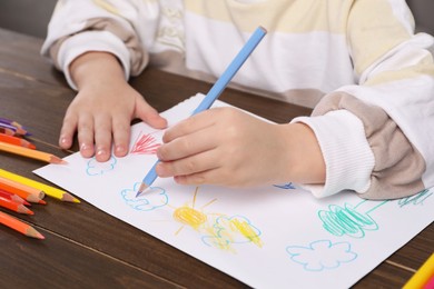 Photo of Little boy drawing with pencil at wooden table, closeup. Child`s art