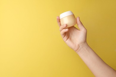 Photo of Woman holding jar of face cream on yellow background, closeup. Space for text