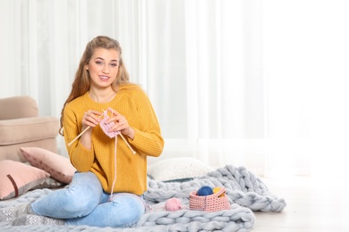 Photo of Young woman in cozy warm sweater knitting with needles on floor at home. Space for text