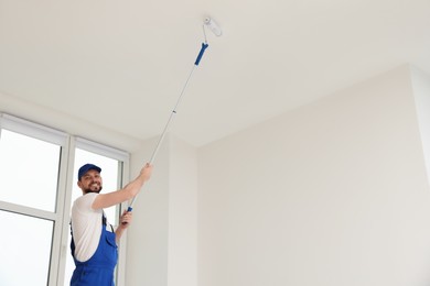 Photo of Worker in uniform painting ceiling with roller indoors. Space for text