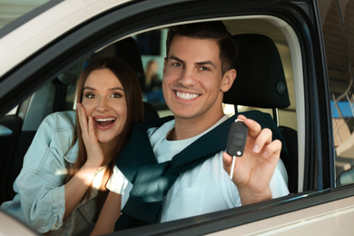 Happy couple with car key sitting in modern auto at dealership